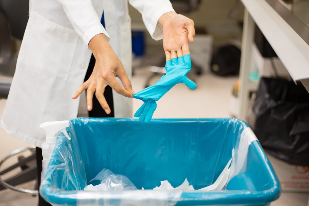 Doctor putting plastic gloves in clinical waste bin