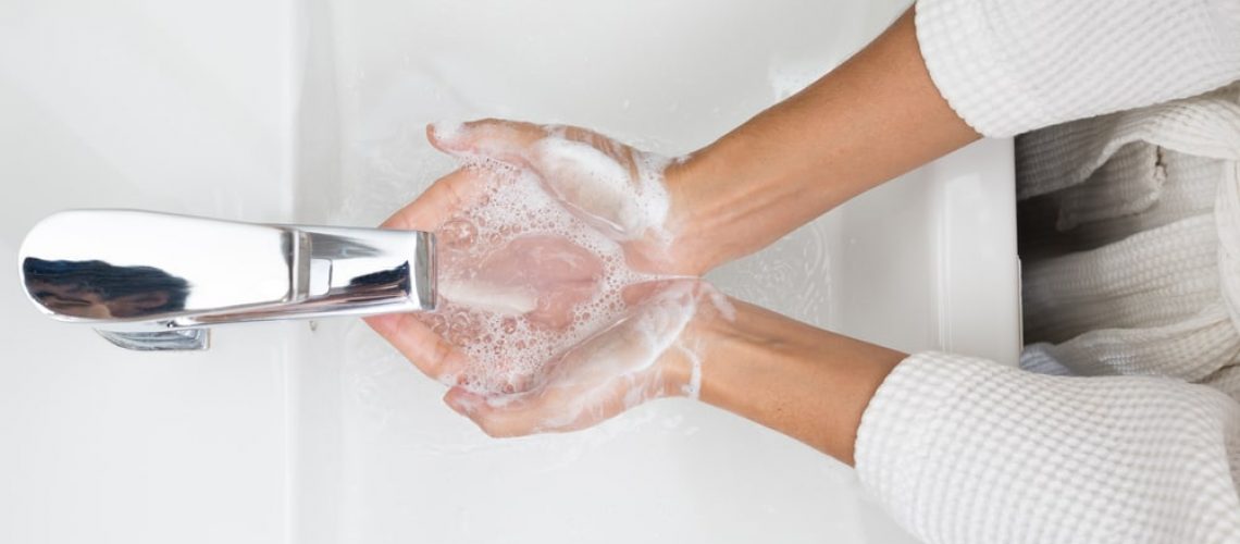 Person washing hands with water and soap in bathroom sink